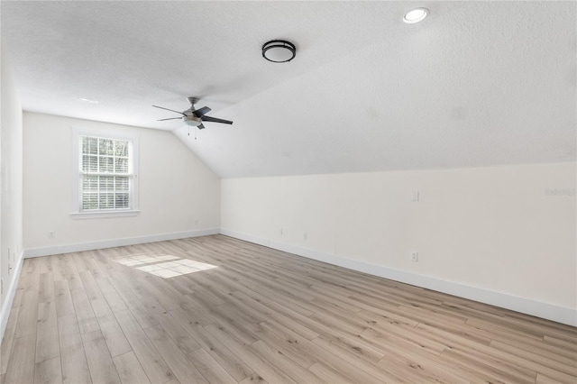 additional living space with a textured ceiling, ceiling fan, vaulted ceiling, and light hardwood / wood-style floors