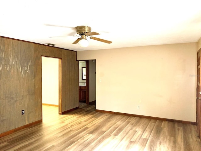 spare room with ceiling fan, light hardwood / wood-style floors, and wood walls