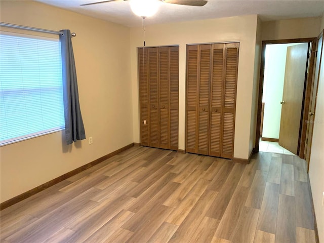 unfurnished bedroom with two closets, light hardwood / wood-style floors, and ceiling fan