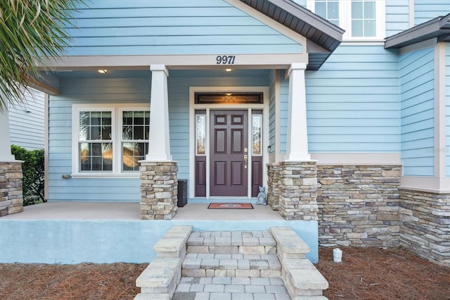 view of exterior entry featuring stone siding and a porch