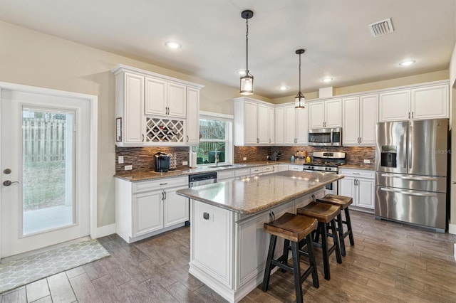 kitchen with appliances with stainless steel finishes, visible vents, white cabinetry, and wood finished floors