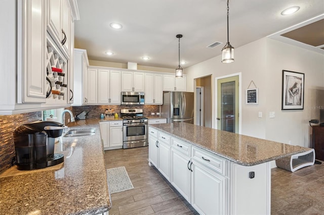 kitchen with white cabinets, stainless steel appliances, decorative light fixtures, and a kitchen island