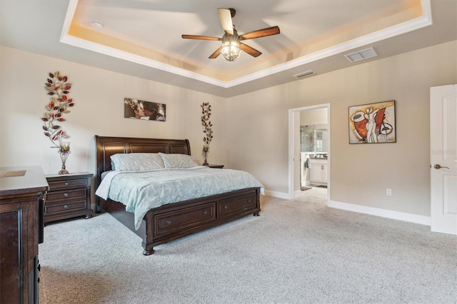 bedroom featuring ensuite bath, a tray ceiling, crown molding, ceiling fan, and light carpet