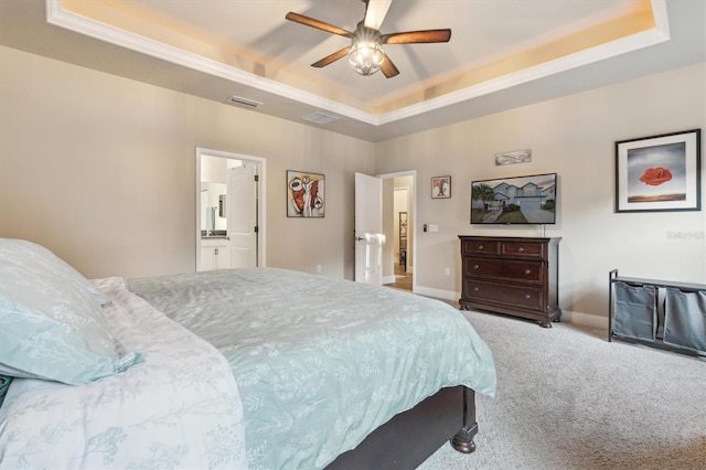 bedroom featuring a raised ceiling, ceiling fan, ensuite bath, and light colored carpet