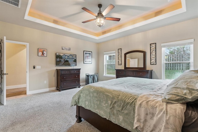 bedroom with a raised ceiling, light colored carpet, ceiling fan, and multiple windows