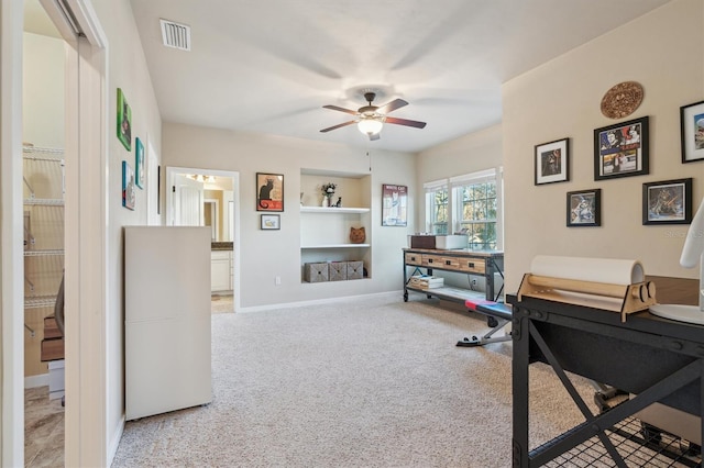 office area featuring built in shelves, light carpet, visible vents, baseboards, and a ceiling fan