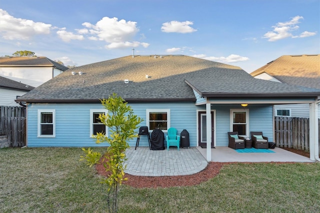 back of house with a shingled roof, a patio area, a lawn, and fence