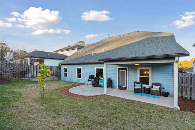 back of house featuring roof with shingles, a patio area, a yard, and fence