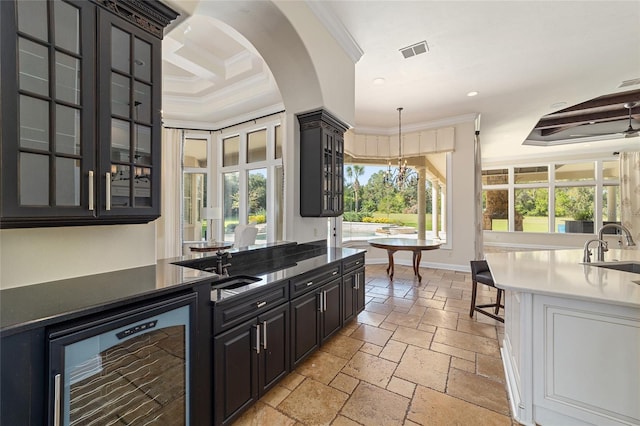 kitchen featuring wine cooler, crown molding, sink, and hanging light fixtures