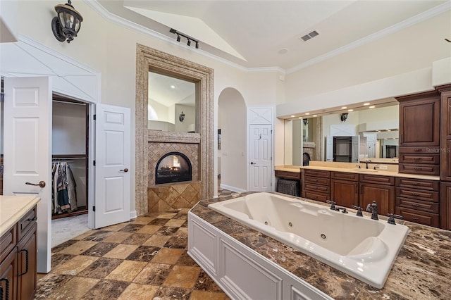 bathroom featuring a tiled fireplace, crown molding, vanity, and lofted ceiling