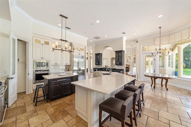 kitchen with a kitchen breakfast bar, built in appliances, a large island with sink, pendant lighting, and ornamental molding