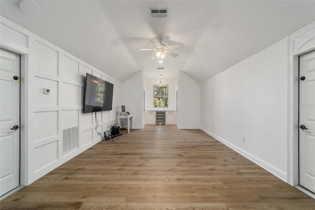 unfurnished living room with ceiling fan, light wood-type flooring, wine cooler, and vaulted ceiling