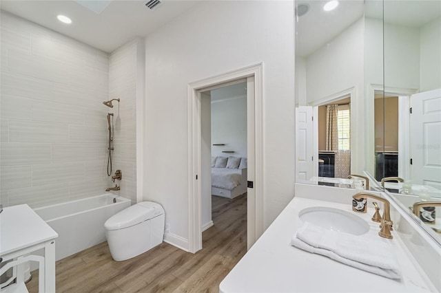 full bathroom with hardwood / wood-style floors, vanity, tiled shower / bath combo, and toilet