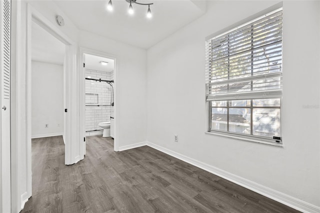 unfurnished bedroom featuring connected bathroom, a closet, dark hardwood / wood-style flooring, and multiple windows