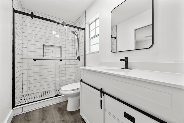 bathroom with hardwood / wood-style floors, vanity, toilet, and a shower with shower door