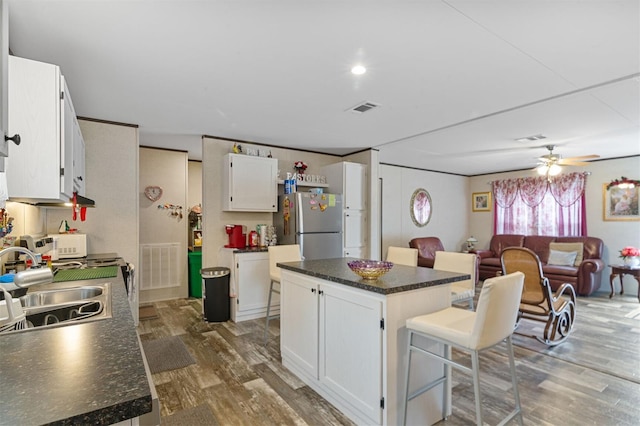 kitchen with white cabinets, stainless steel fridge, a kitchen island, and dark wood-type flooring