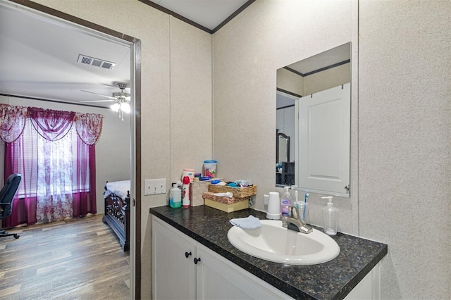 bathroom featuring ceiling fan, vanity, ornamental molding, and hardwood / wood-style flooring