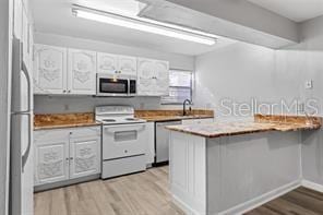 kitchen with white cabinetry, kitchen peninsula, appliances with stainless steel finishes, and light hardwood / wood-style flooring