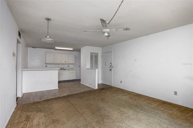 unfurnished living room with dark colored carpet, a textured ceiling, ceiling fan, and sink