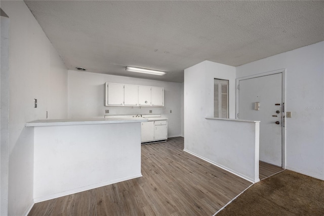 kitchen with kitchen peninsula, a textured ceiling, light hardwood / wood-style floors, and white cabinets