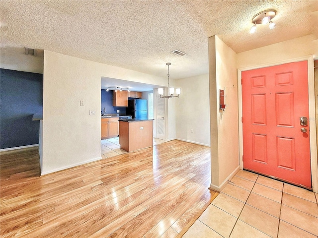 entrance foyer featuring a chandelier, a textured ceiling, light hardwood / wood-style flooring, and sink