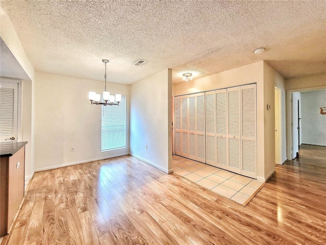 unfurnished dining area featuring an inviting chandelier, a textured ceiling, and light wood-type flooring