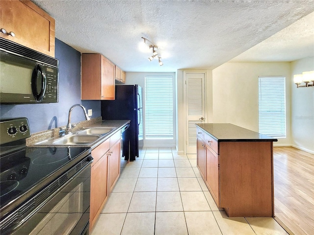 kitchen with a center island, black appliances, sink, light tile patterned floors, and a textured ceiling