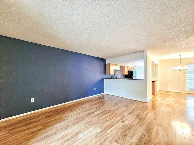 unfurnished living room featuring a chandelier, a textured ceiling, and light hardwood / wood-style flooring