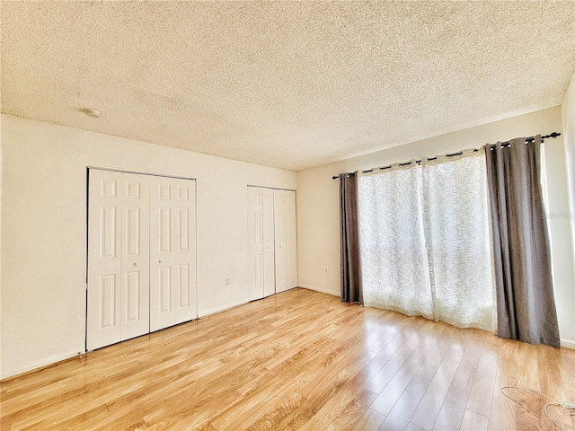 unfurnished bedroom with multiple closets, a textured ceiling, and light hardwood / wood-style flooring