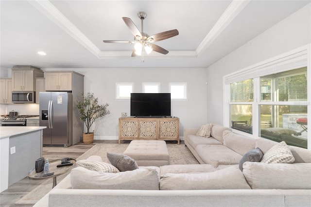 living room with light wood-type flooring, a tray ceiling, a wealth of natural light, and ceiling fan