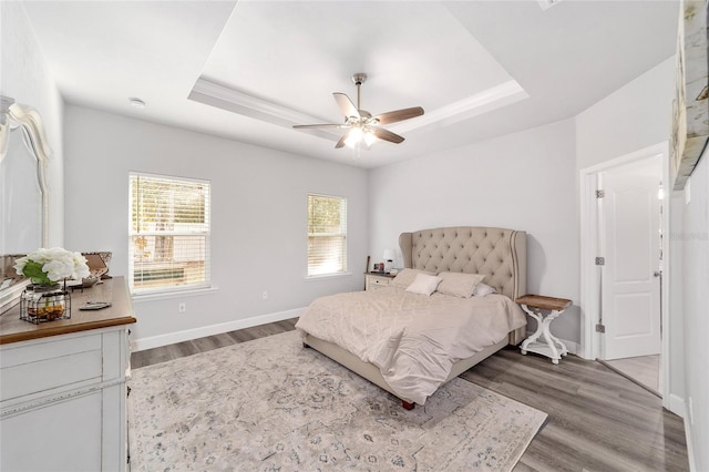 bedroom with wood-type flooring, a raised ceiling, and ceiling fan