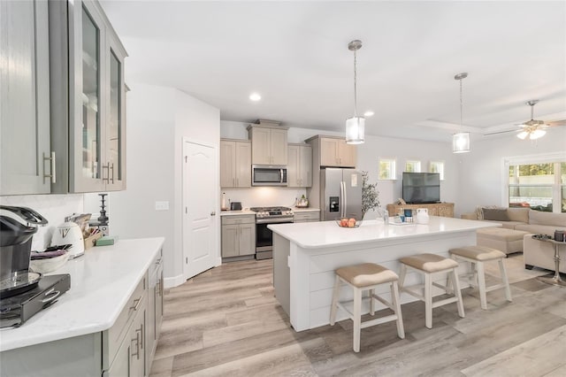 kitchen with appliances with stainless steel finishes, a kitchen breakfast bar, ceiling fan, decorative light fixtures, and light hardwood / wood-style flooring