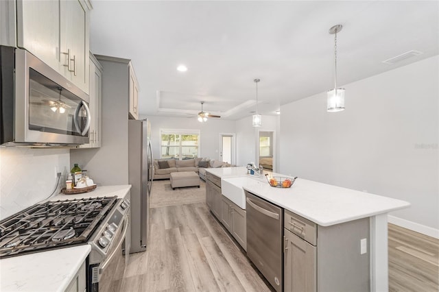 kitchen with stainless steel appliances, pendant lighting, gray cabinets, decorative backsplash, and light wood-type flooring