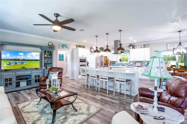 living room with hardwood / wood-style floors, ceiling fan with notable chandelier, and crown molding