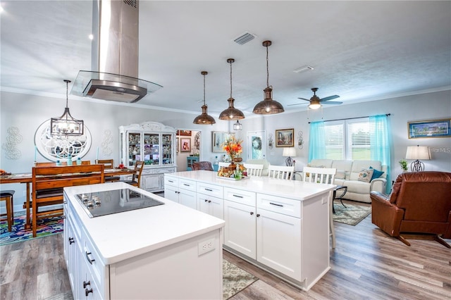 kitchen with island exhaust hood, light hardwood / wood-style floors, decorative light fixtures, a center island with sink, and white cabinets