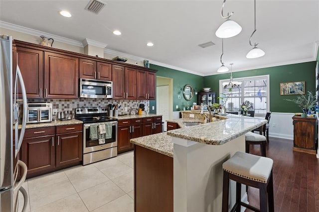 kitchen featuring stainless steel appliances, crown molding, sink, decorative light fixtures, and an island with sink