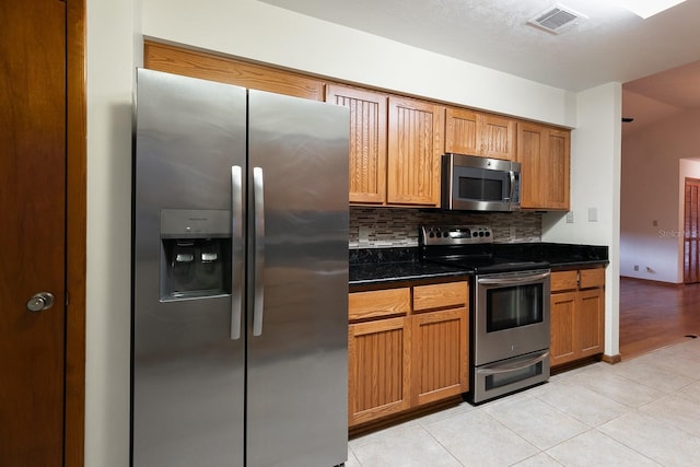 kitchen with light tile patterned floors, backsplash, stainless steel appliances, and dark stone countertops