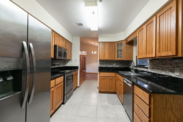 kitchen with dark stone counters, sink, light tile patterned flooring, stainless steel appliances, and a chandelier