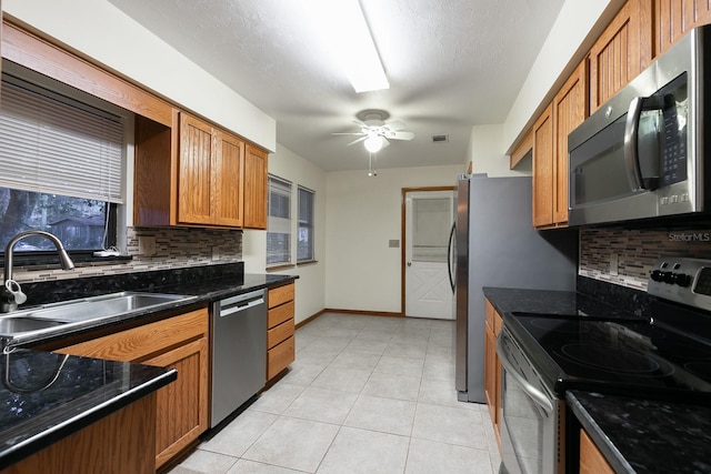 kitchen featuring backsplash, stainless steel appliances, ceiling fan, sink, and dark stone countertops