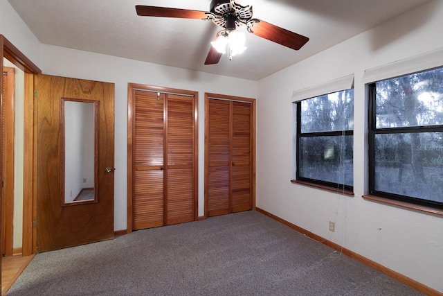 unfurnished bedroom with carpet flooring, ceiling fan, and two closets