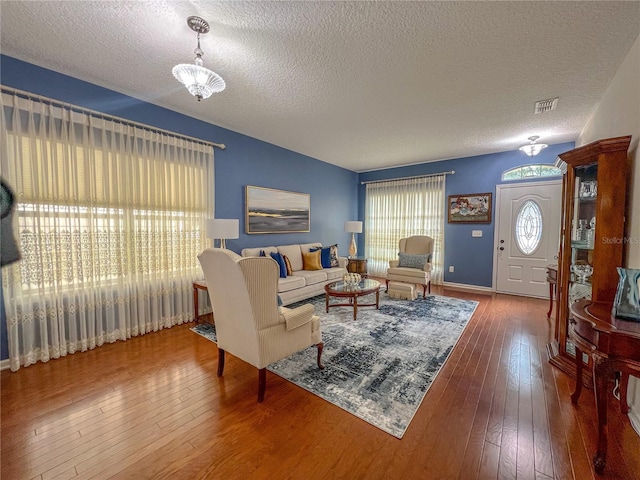 living room with hardwood / wood-style floors, a healthy amount of sunlight, a textured ceiling, and an inviting chandelier