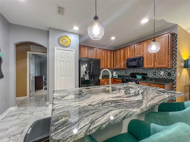 kitchen featuring a kitchen island with sink, black appliances, sink, hanging light fixtures, and tasteful backsplash