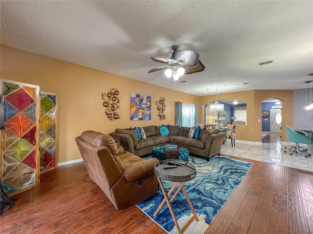 living room featuring ceiling fan with notable chandelier, wood-type flooring, and a textured ceiling