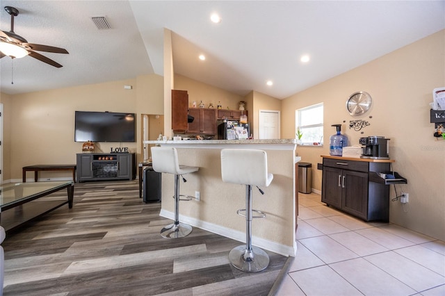 kitchen with a kitchen breakfast bar, black fridge, kitchen peninsula, lofted ceiling, and light wood-type flooring