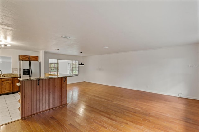 kitchen with stainless steel refrigerator with ice dispenser, a breakfast bar, pendant lighting, light hardwood / wood-style floors, and a kitchen island