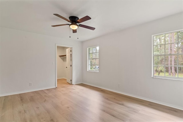 unfurnished bedroom featuring light wood-type flooring, a spacious closet, multiple windows, and ceiling fan