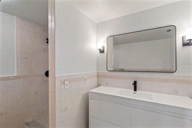 bathroom featuring vanity, a tile shower, and tile walls