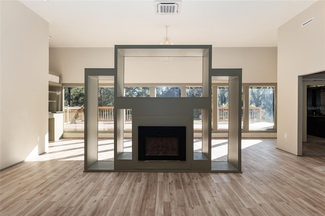 unfurnished living room with light wood-type flooring, a high ceiling, and a notable chandelier