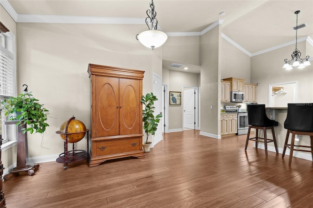 entryway with a notable chandelier, wood-type flooring, ornamental molding, and high vaulted ceiling