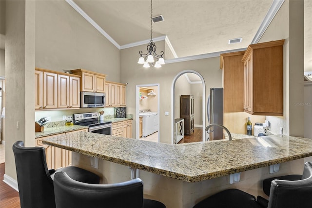 kitchen with pendant lighting, independent washer and dryer, appliances with stainless steel finishes, a notable chandelier, and a breakfast bar area